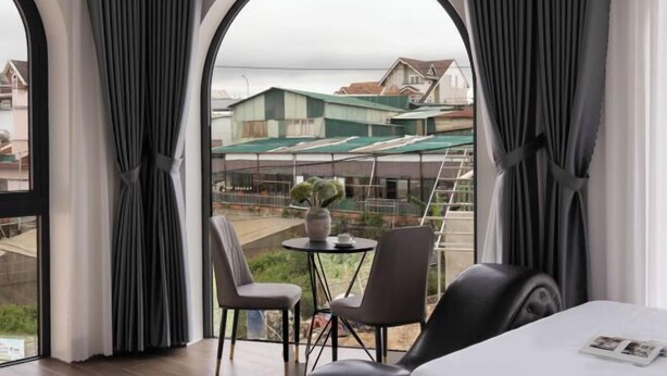 A hotel room with a large arched window, a round table with chairs, and a bed with a magazine on it. - Anteaus Hotel & Apartment Da Lat (Dalat)