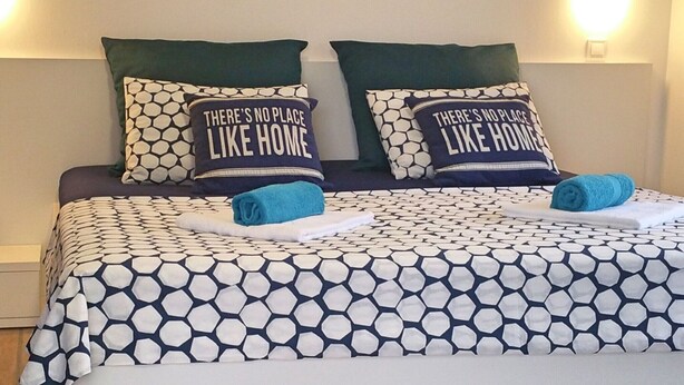 A bed with a patterned bedspread and two matching pillows with the text "There's no place like home." - Apartments Mateo - One Bedroom Apartment - Blue (Vodice)