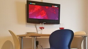 A room with a flat-screen TV mounted on the wall, a wooden table, two chairs, and a wine glass. - Apartments Mateo - One Bedroom Apartment - Blue (Vodice)