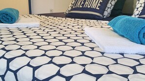 A bed with a geometric patterned bedspread, two rolled towels, and a pillow with the text "THERE'S NO PLACE LIKE HOME". - Apartments Mateo - One Bedroom Apartment - Blue (Vodice)