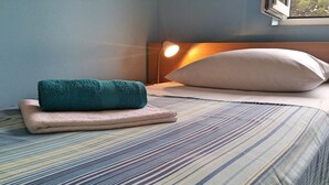 A neatly made bed with a striped bedspread, a teal towel, and a beige pillow.