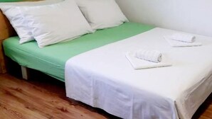 A single bed with a green mattress and white bedding, a wooden headboard, and two rolled towels on the footboard.