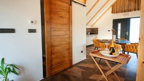 Un interior moderno con una puerta corredera de madera, un comedor con mesa para dos, y una cocina al fondo.