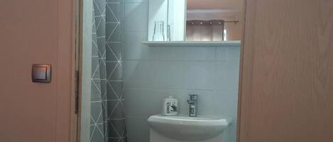 A bathroom with a white sink, a mirror above it, and a shower area with a geometric tile pattern.