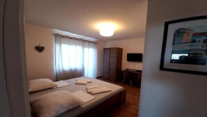Ein Hotelzimmer mit Bett, Schreibtisch, Sessel, Fernseher und einem Bild an der Wand.