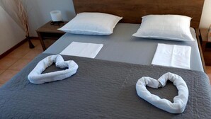 Ein ordentlich bezogenes Bett mit einer grauen Steudecke, zwei weißen Kissen und zwei herzförmigen Handtüchern.