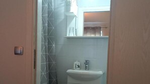 Ein Badezimmer mit einem weißen Waschbecken, einem Spiegel darüber und einem Duschbereich mit einem geometrischen Fliesenmuster.