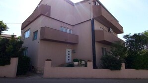 Ein zweigeschossiges Gebäude mit flachem Dach, einem zentralen Eingang mit einer Tür und einem kleinen Balkon im Erdgeschoss.