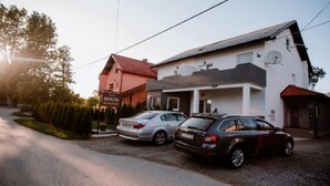 Un bâtiment à deux étages avec une enseigne indiquant « HOUSE KARAKAS ». Deux voitures sont garées devant.