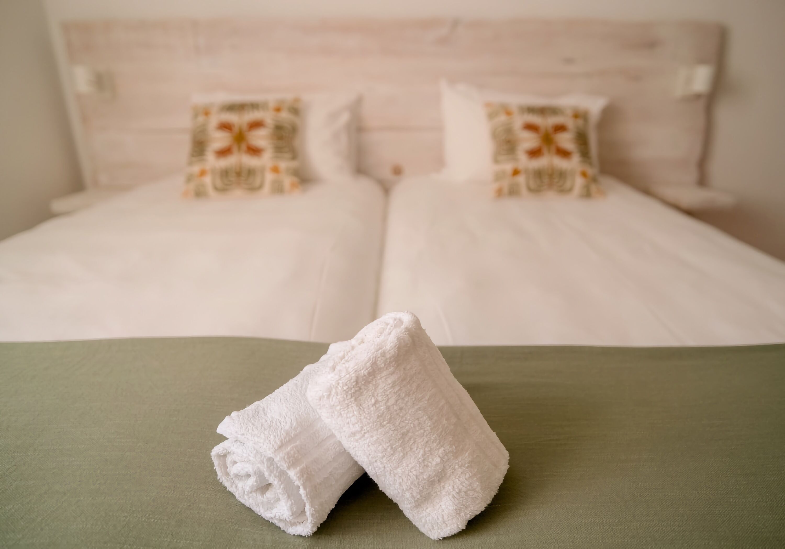 Cama bem arrumada com lençóis brancos e duas almofadas decorativas.