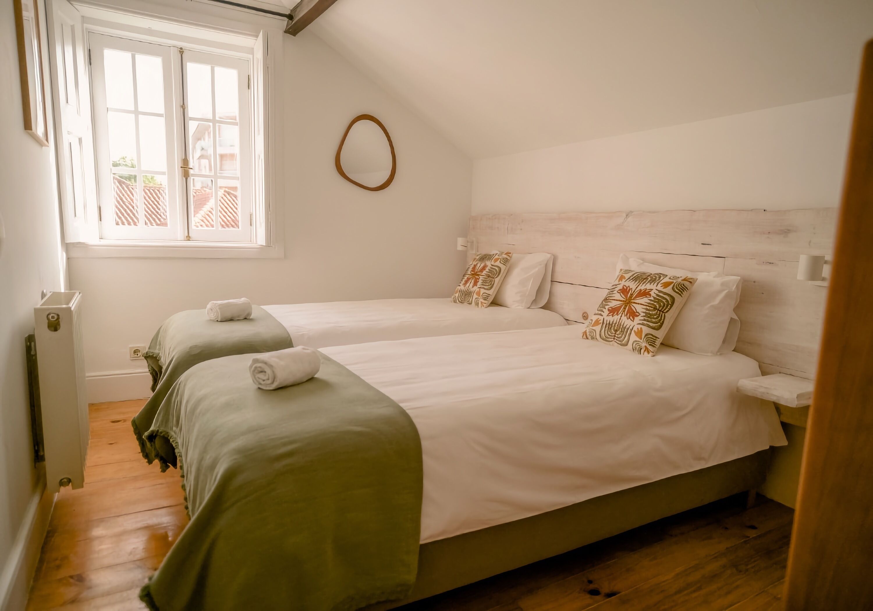 A bedroom with two beds, a window, and a wooden floor.