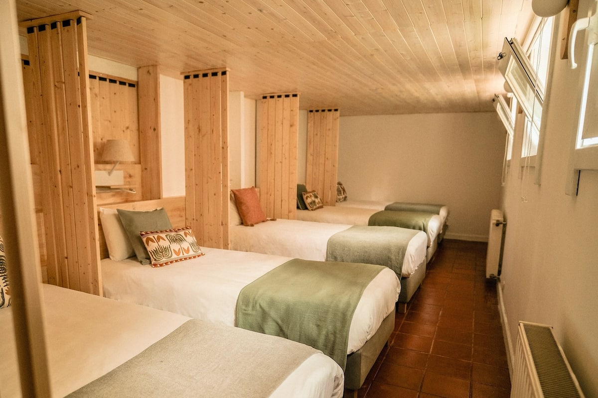 A room with four beds arranged in a row, wooden paneling on the walls, and a radiator on the right wall.