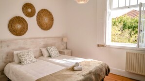 A bedroom with a large bed, a nightstand, a wall-mounted lamp, and a view of greenery outside. - Porto Surf Lodge (Porto)