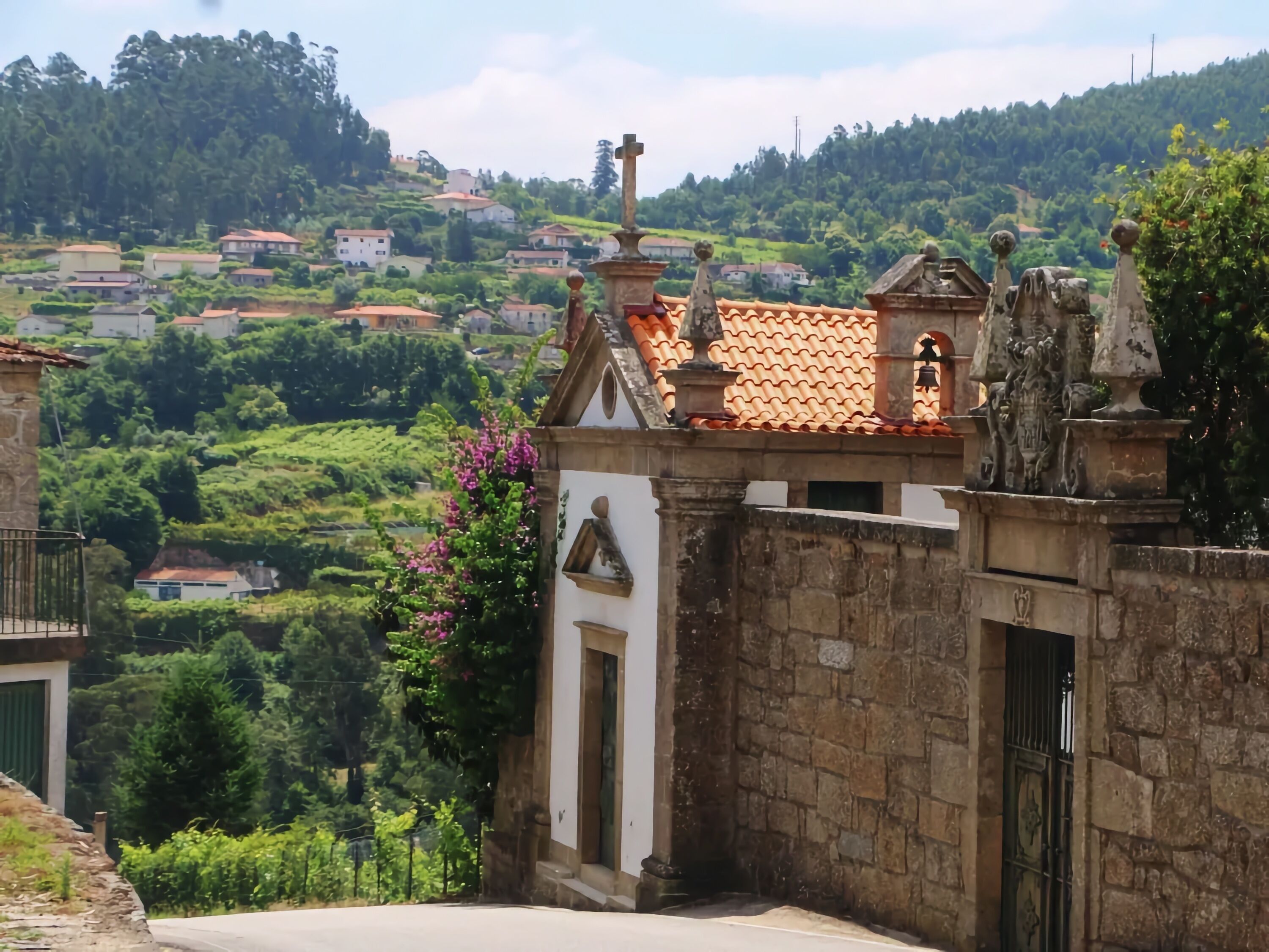A stone building with a tiled roof, a small bell tower, and a gate.