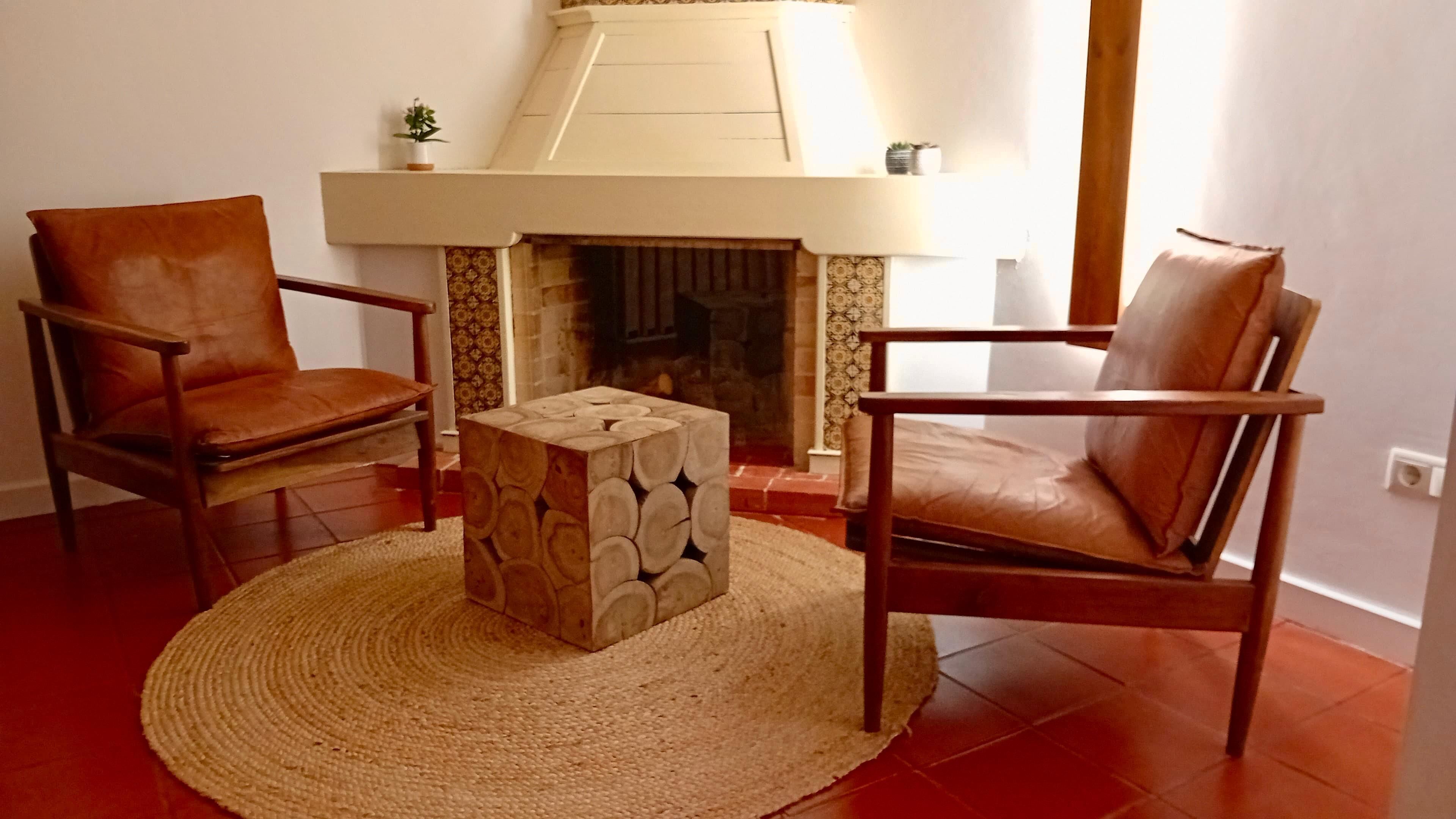 A living room with a fireplace, two leather chairs, and a woven rug.