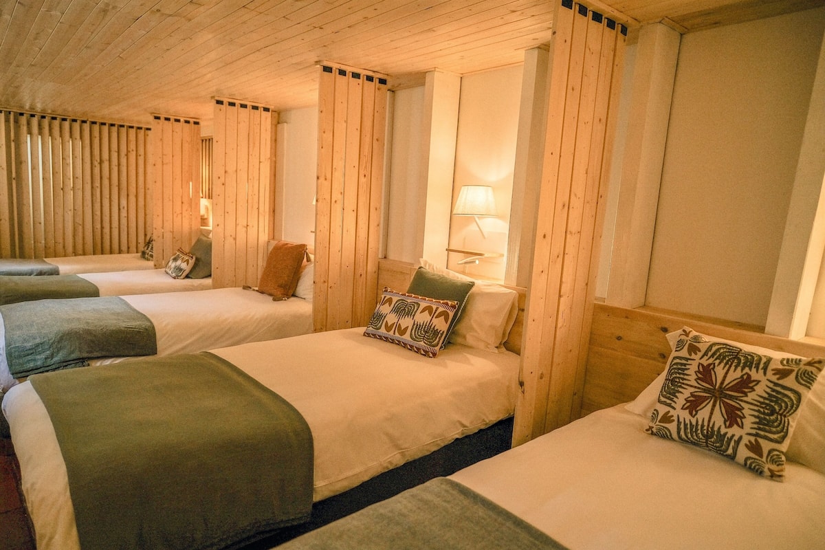 A room with three beds, wooden walls, and a lamp on the wall.