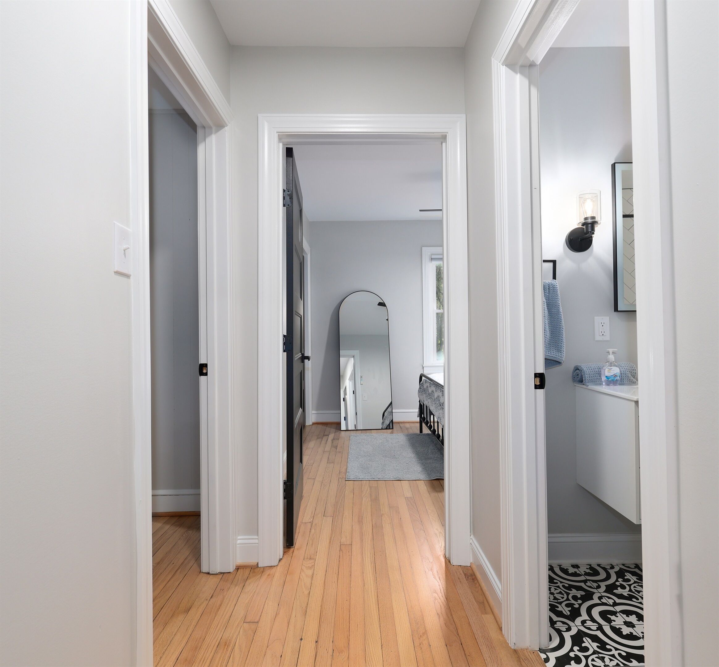 A hallway with a wooden floor, white walls, and a door leading to a bedroom.
