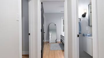 A hallway with a wooden floor, white walls, and a door leading to a bedroom.