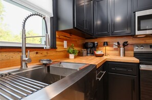 Una cocina moderna con un lavamanos de acero inoxidable, encimera de madera y armarios negros.
