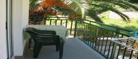 A balcony with a table and chairs, surrounded by a green railing and palm trees.
