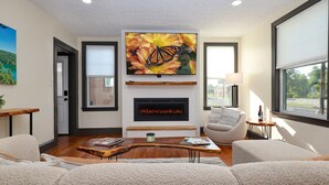 A modern living room with a fireplace, comfortable seating, and a large TV mounted above it. - Luxury 3BR Getaway • Steps From the River access (Bassett)