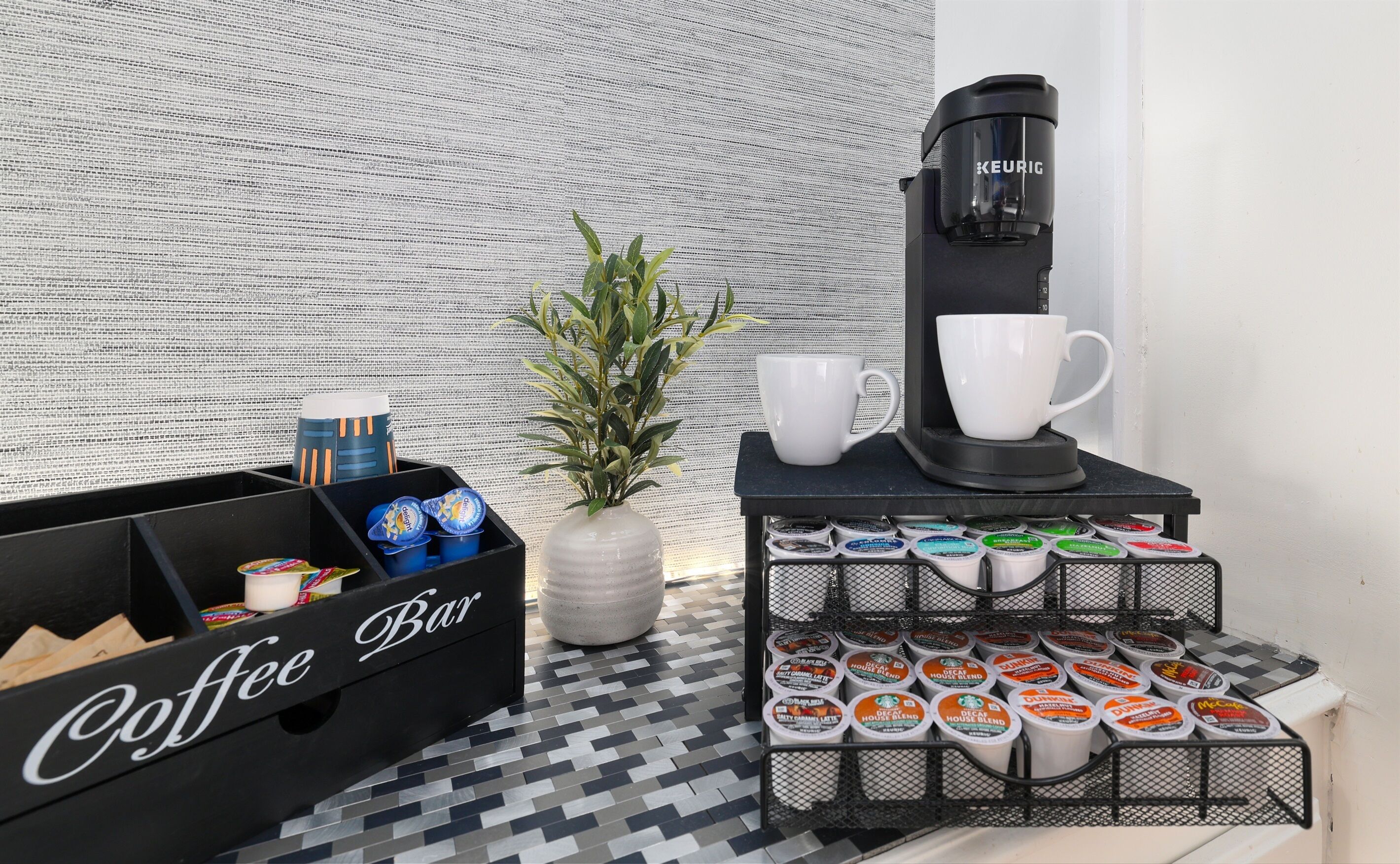 Een koffiehoek met een Keurig koffieapparaat, een koffiebar en diverse koffiekapsules.