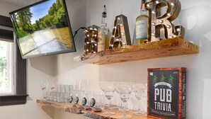 A bar area with shelves displaying bottles, glasses, and a PIER trivia game box. - Luxury 3BR Getaway • Steps From the River access (Bassett)