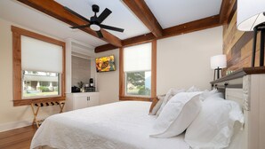A bedroom with a large bed, wooden beams, a ceiling fan, and a window with a view of the outside. - Luxury 3BR Getaway • Steps From the River access (Bassett)