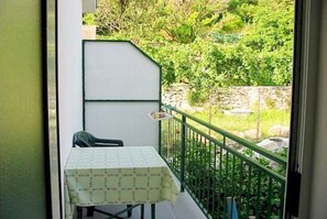 Un balcone con tavolo e sedia, ringhiera verde e vista su vegetazione e un muro in pietra.