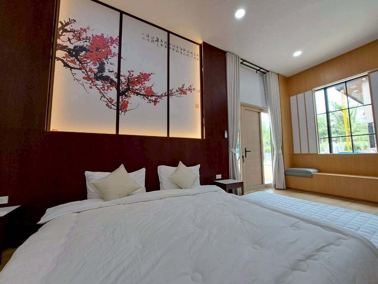 A large bed with white bedding, a wall-mounted artwork, a bedside table, and a window with curtains.