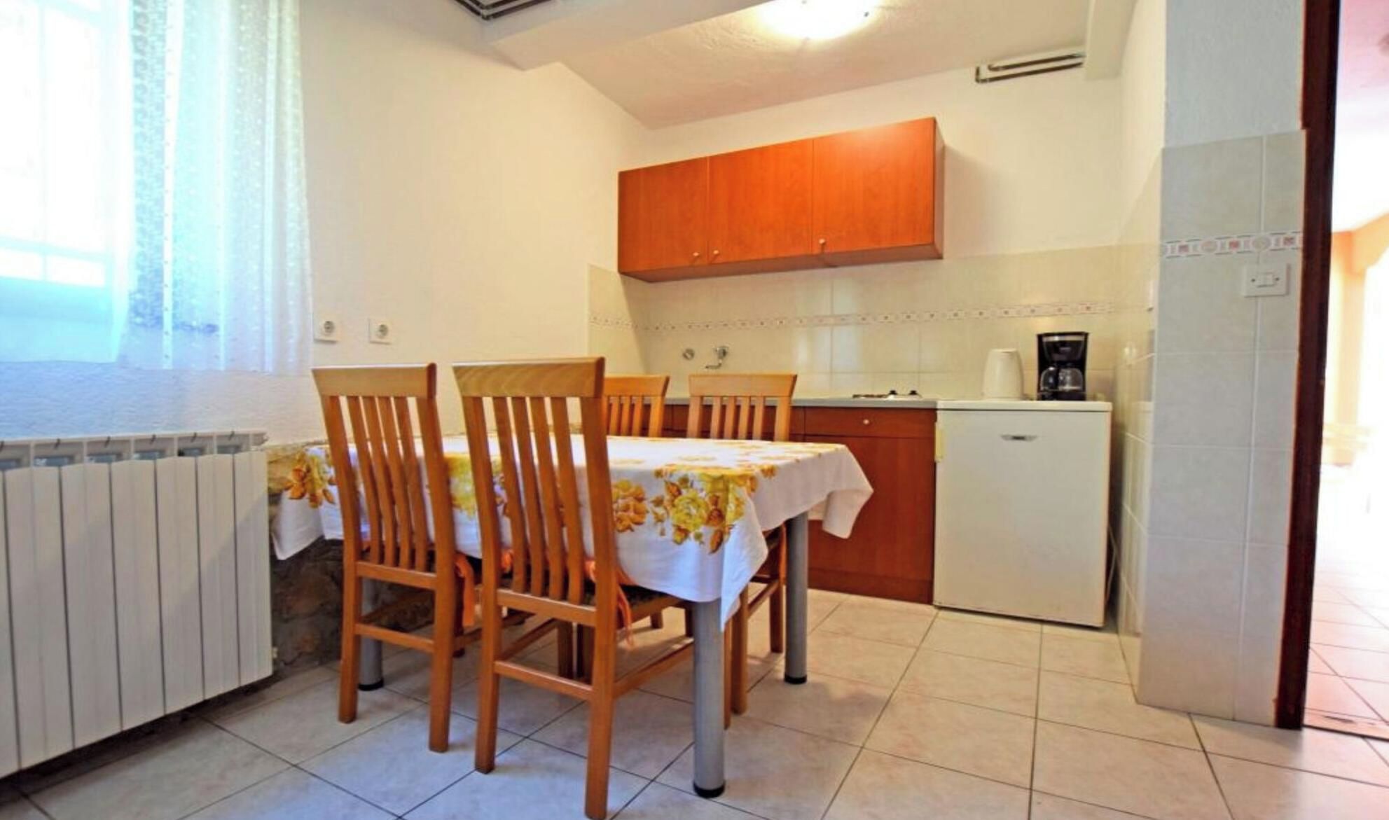 A compact kitchen with wooden cabinets, a small refrigerator, and a dining table with chairs.