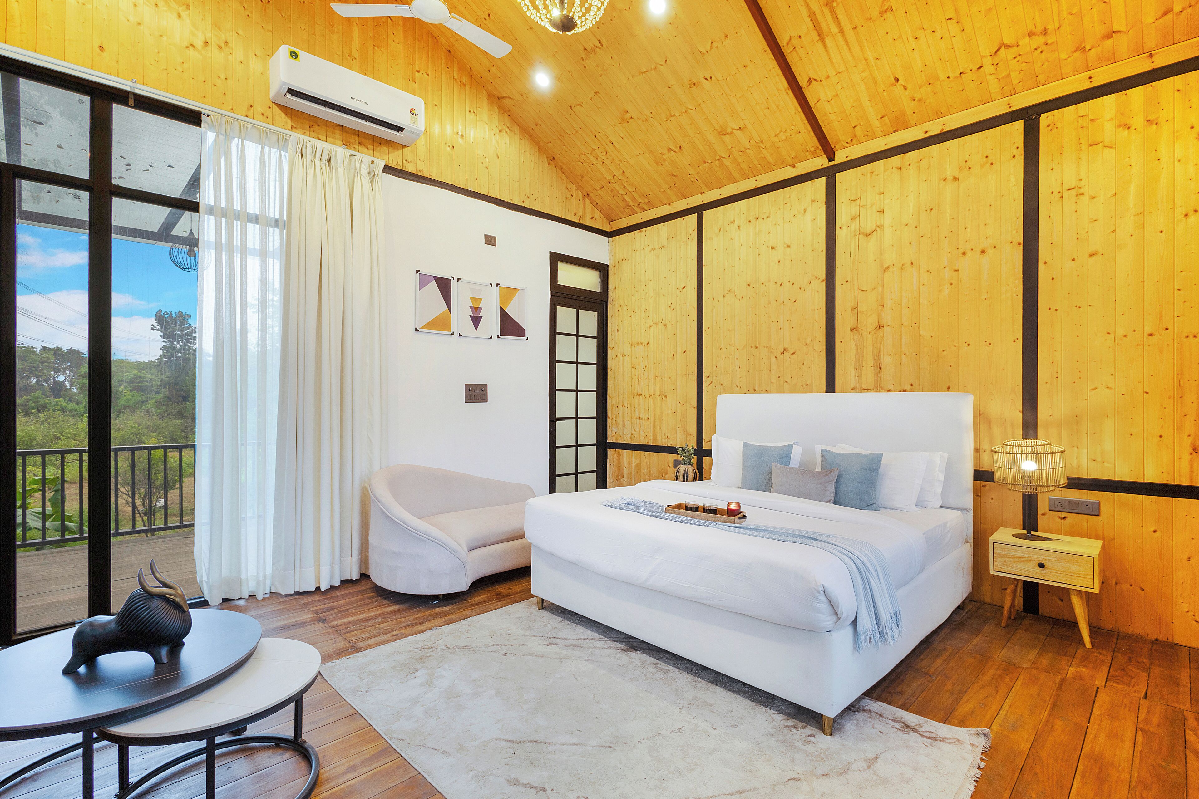 A bedroom with a large bed, a bedside table, a chair, and a view of the outdoors.