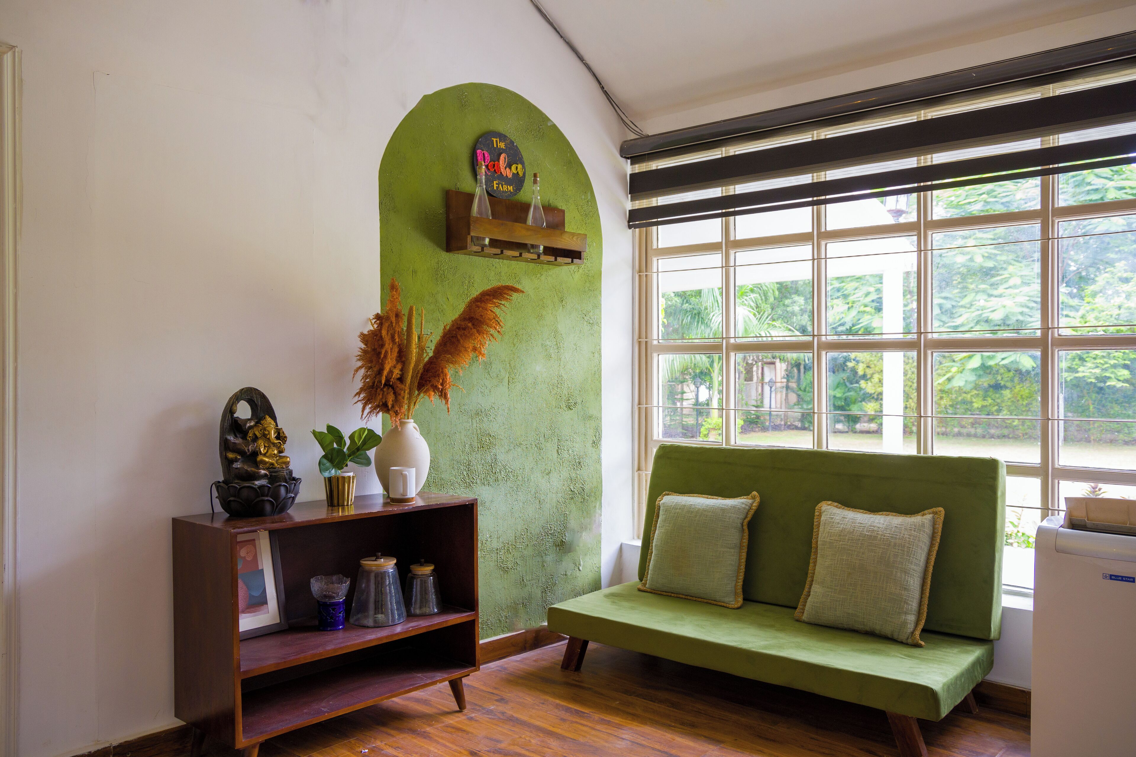 A room with a green sofa, a wooden shelf with decorative items, and a window with a view of greenery.
