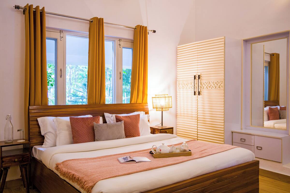 A neatly arranged bedroom with a large bed, a bedside table, a nightstand, a mirror, and a window with curtains.