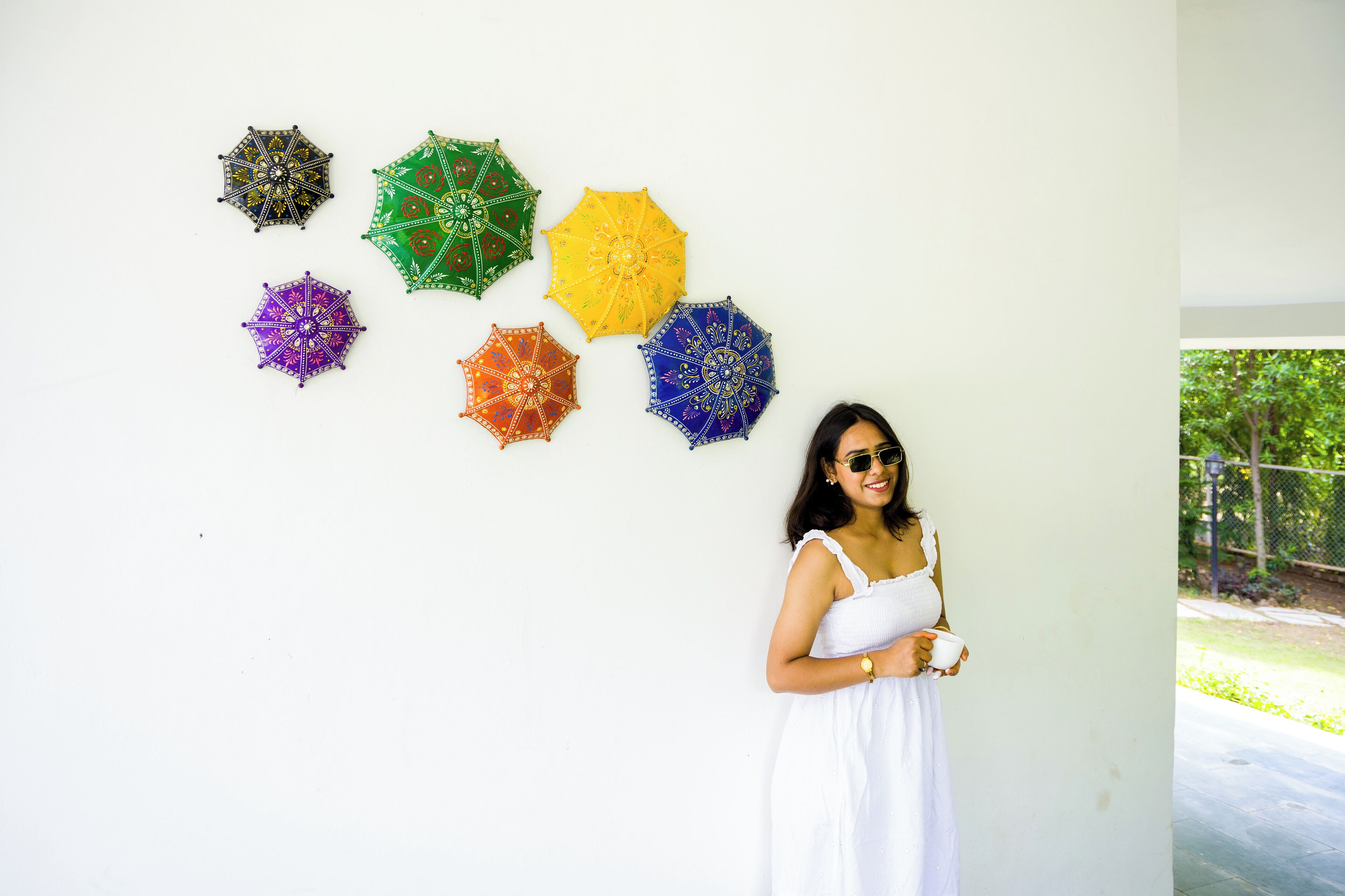 A person standing next to a wall with six colorful umbrellas.