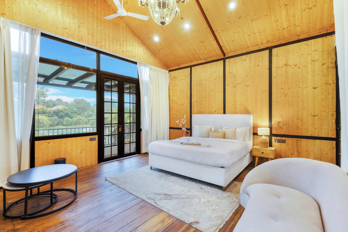 A bedroom with a large bed, a nightstand, a chair, and a view of the outdoors through a sliding door.