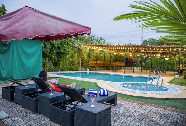 Zona de piscina con sillas de descanso, un espacio de estar techado y una pequeña fuente.