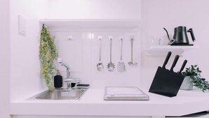 A kitchen with a white countertop, a sink, a knife block, a kettle, and utensils hanging on the wall. - Minimalist Loft 5: Namba Compact Studio & 24/7 Gym (Osaka)