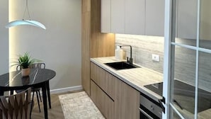 A modern kitchen with a dining area, featuring a round table, chairs, a hanging light fixture, and built-in appliances. - Downtown Shkodra Apartment (Shkodër)