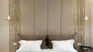 A neatly made bed with white linens and two rolled towels, a headboard with vertical panels, and two wall-mounted lamps.