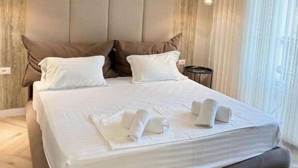 A modern hotel room with a large bed, two bedside tables, and a view of the outdoors through sheer curtains. - Downtown Shkodra Apartment (Shkodër)