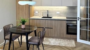 A modern kitchen with wooden cabinets, a central island, and a dining area with a table and chairs. - Downtown Shkodra Apartment (Shkodër)