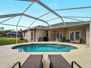 A pool area with a covered patio, lounge chairs, and a screened-in room.
