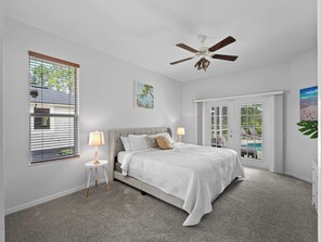 A bedroom with a bed, two bedside lamps, a ceiling fan, a window with blinds, and a door leading to a balcony.