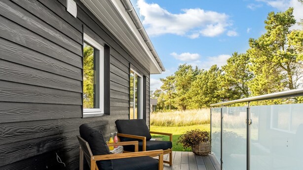En träveranda med två stolar och ett bord, med utsikt över en gräsyta och träd.