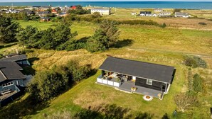 Ett modernt hus med en stor terrass, omgivet av en gräsklädd äng och med utsikt över havet.