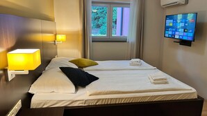 Habitación de hotel con dos camas, televisión, aire acondicionado y ventana con cortinas.