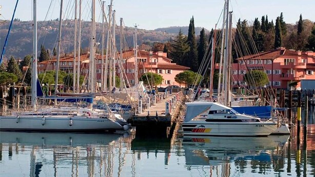 Un puerto deportivo con varias embarcaciones amarradas, rodeado de edificios residenciales y colinas al fondo.