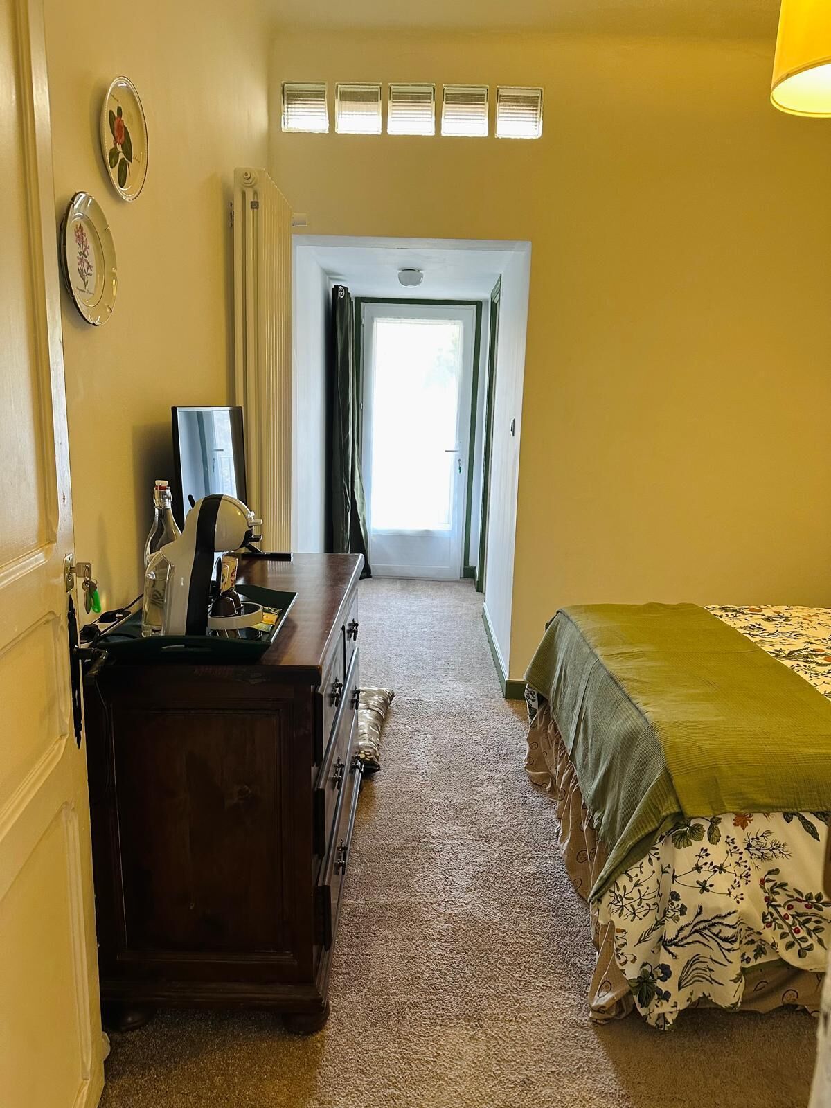 Ein Hotelzimmer mit Bett, Kommode, Spiegel und einem Fenster mit Vorhängen.
