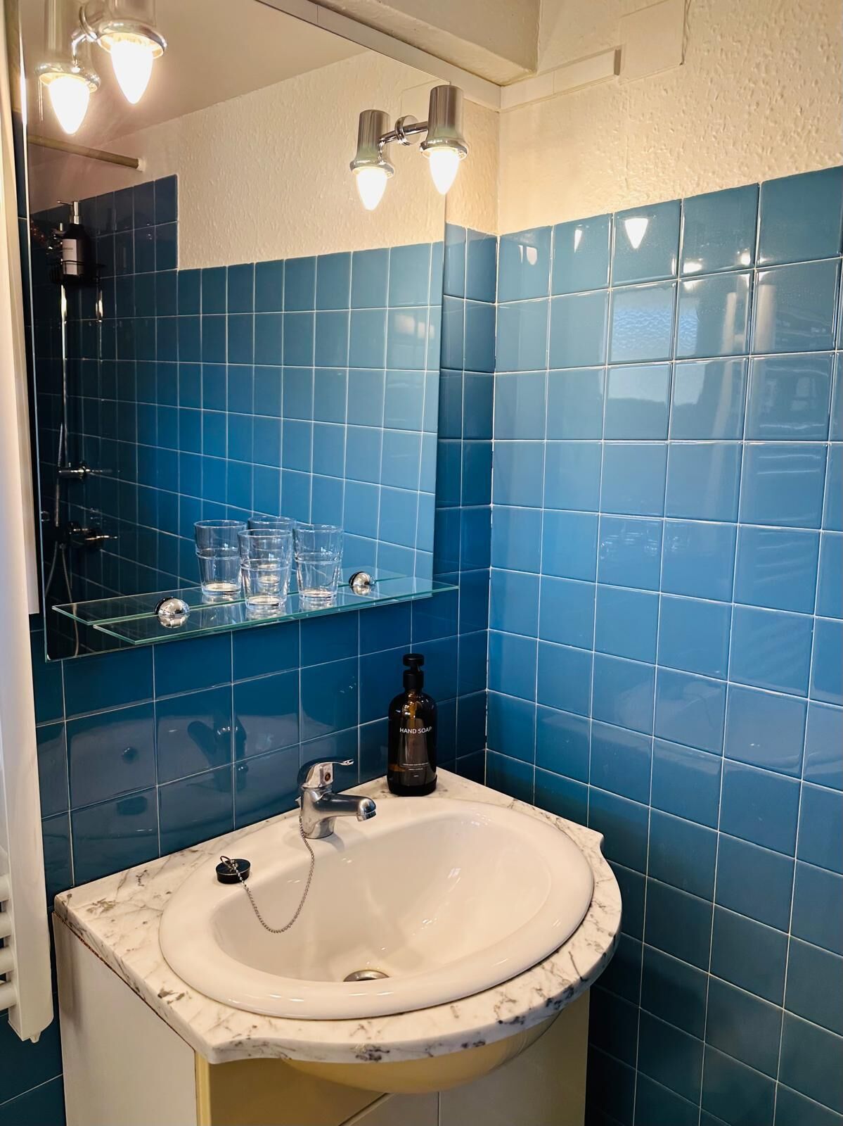 A bathroom with a white sink, blue tiles, and a glass shelf with toiletries.